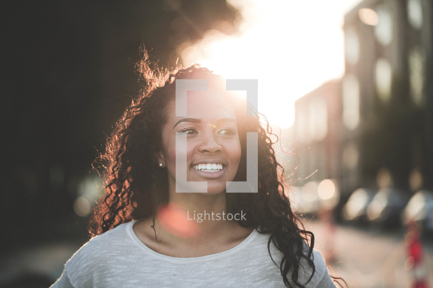 a smiling young African-American woman outdoors under intense sunlight 