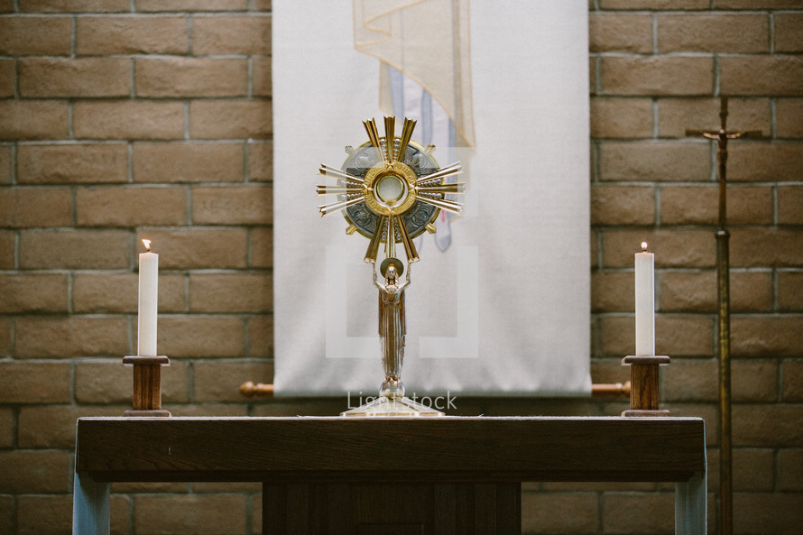 Table with a monstrance and candles in front of a brick wall.