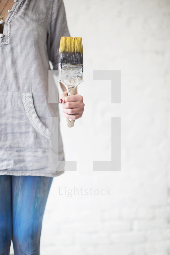 A woman holds a paint brush with yellow paint.