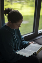 Woman reading bible next to window