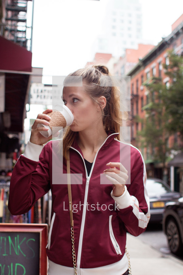 a woman drinking from a paper coffee cup 