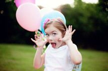 girl child holding balloons making silly faces