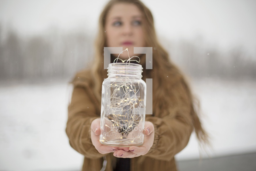 a woman holding a mason jar full of fairy lights 