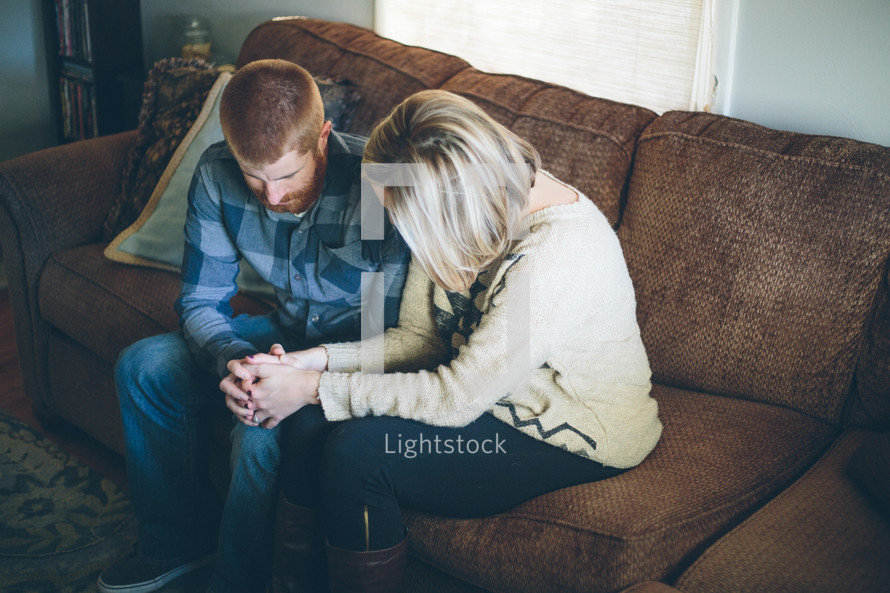 couple praying together on a couch 