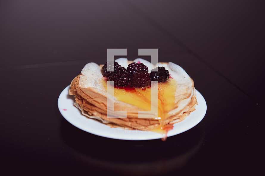 Stack of thin pancakes poured with honey and decorated with fresh blueberries side view with selective focus and dark background with copy space