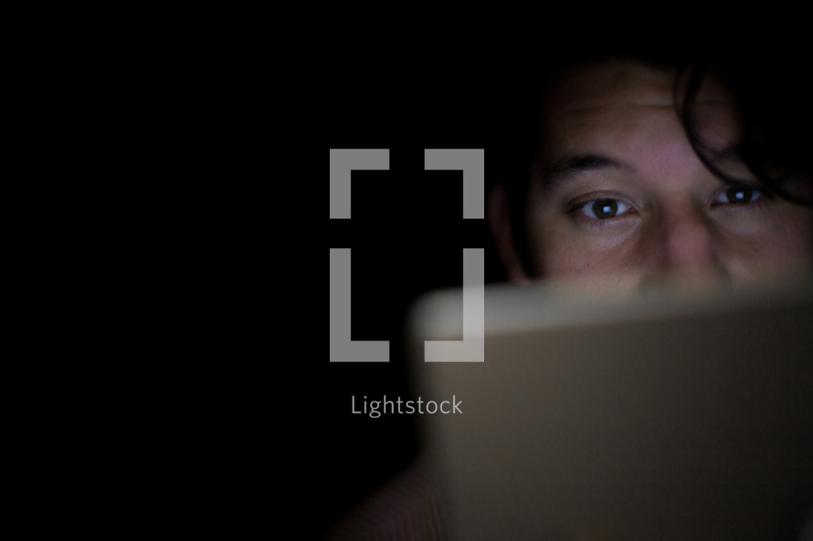 A man's face illuminated by the light of an electronic tablet.