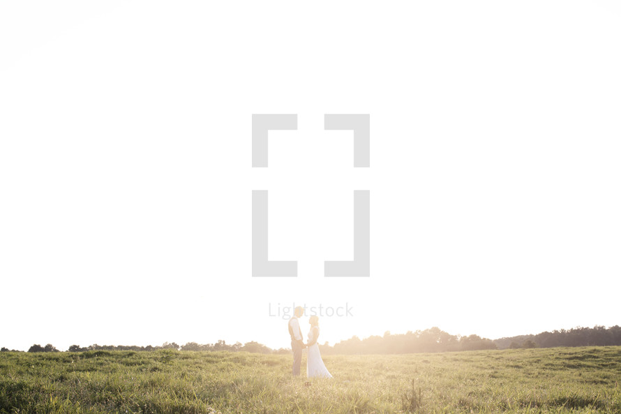 bride and groom standing in intense sunlight in a field 