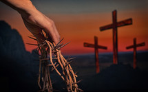Hand holding crown of thorns with three crosses on calvary hill