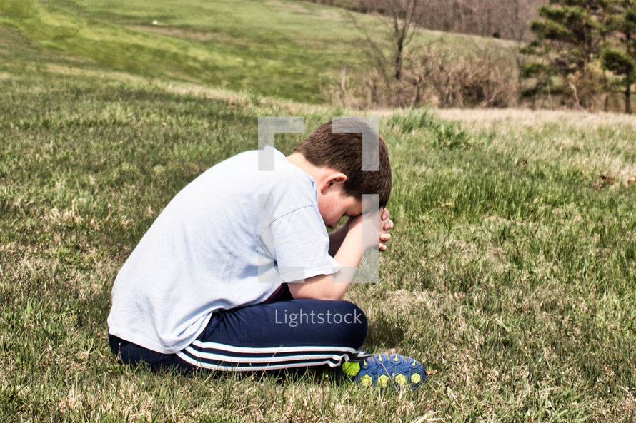 praying boy sitting in grass