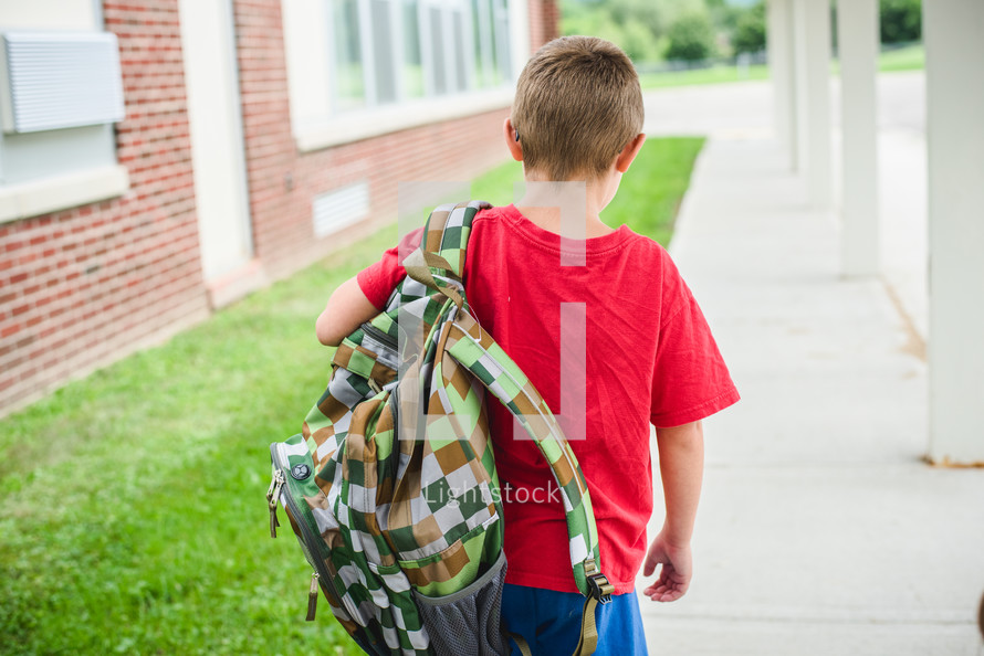 a boy carrying a book bag to school 