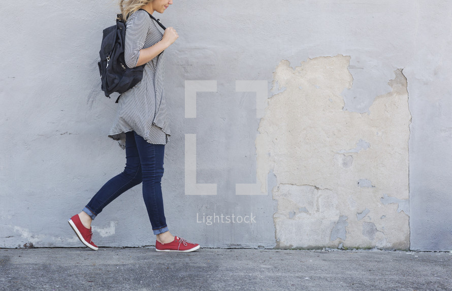 a woman walking on a sidewalk carrying a bag