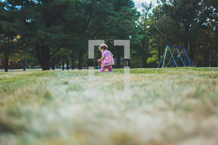 a toddler girl walking in grass on a playground 