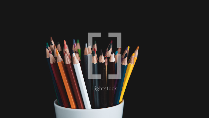 colored pencils in white cup on a black background