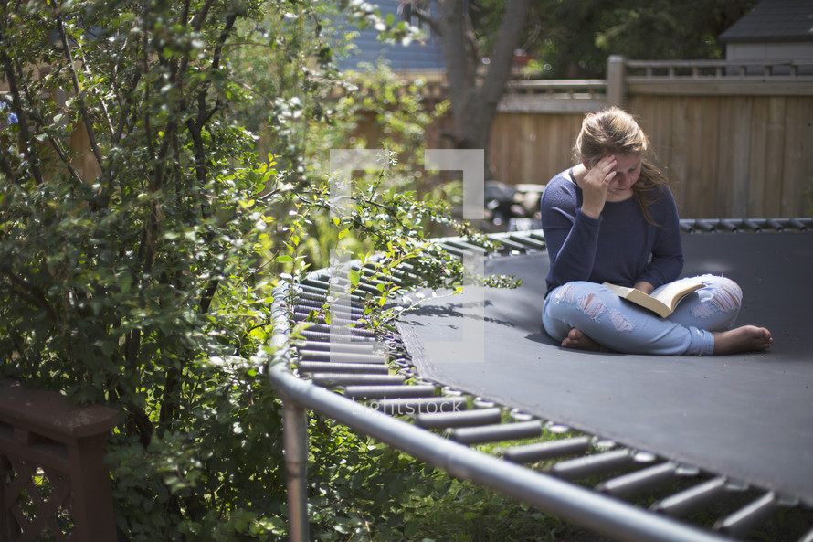 a young teen reading her devotions outside on the trampoline