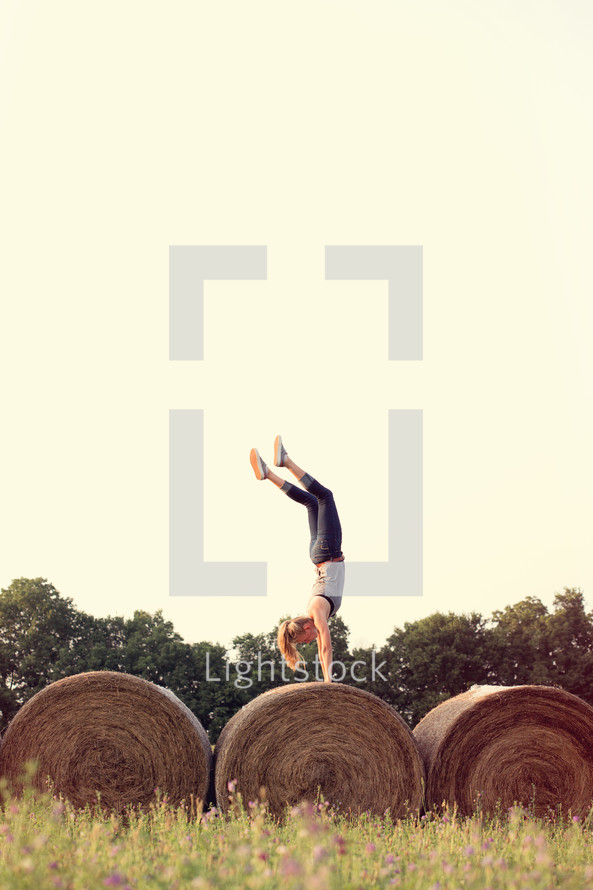 woman doing a handstand on hay bales 