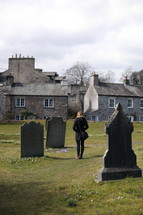 A woman walks away from a cemetery near a stone church.