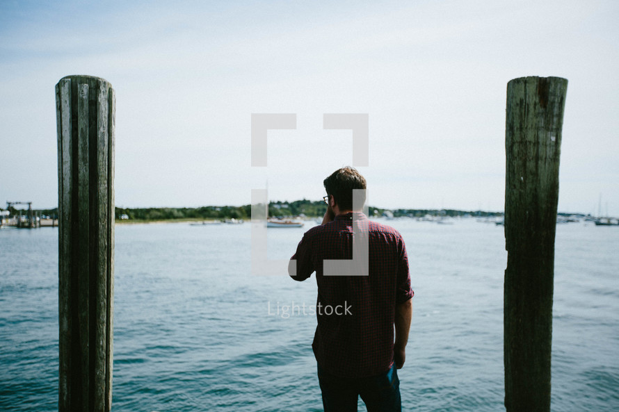 A man standing on a dock looking out at a harbor 