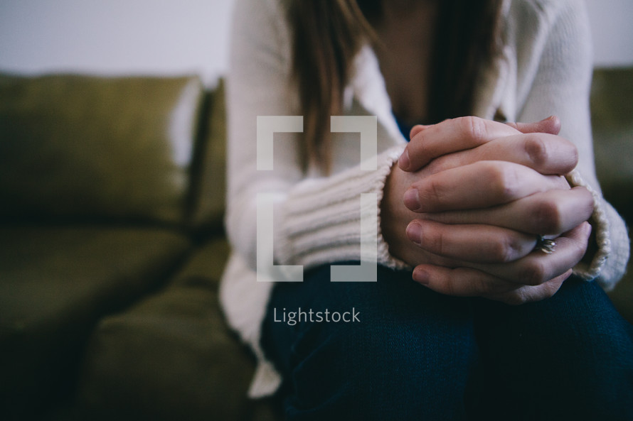 A woman sits with her hands clasped together.