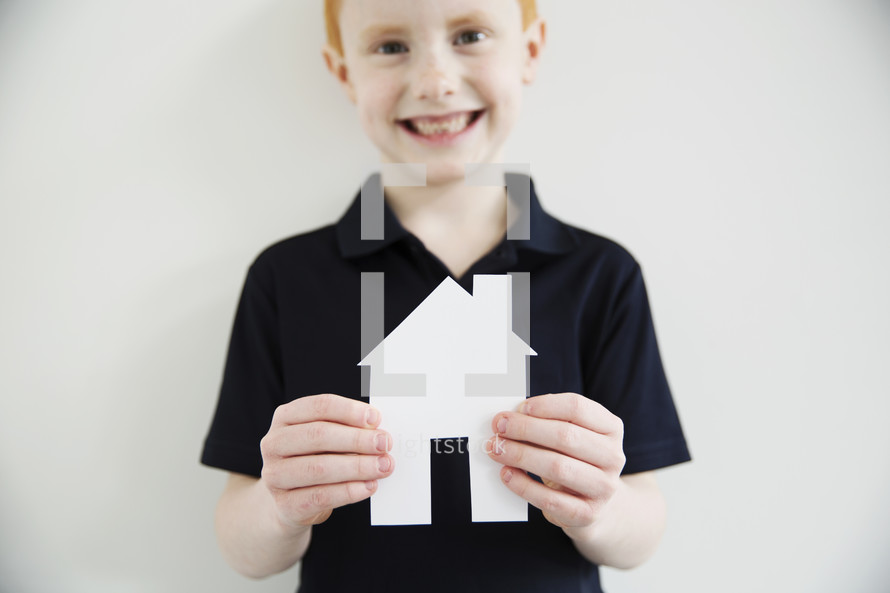 A smiling boy holding a paper cut-out of a house.