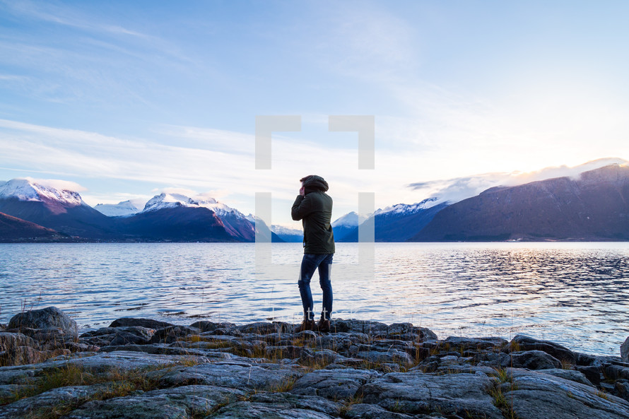 woman standing on rocks on a lake shore looking out at mountains