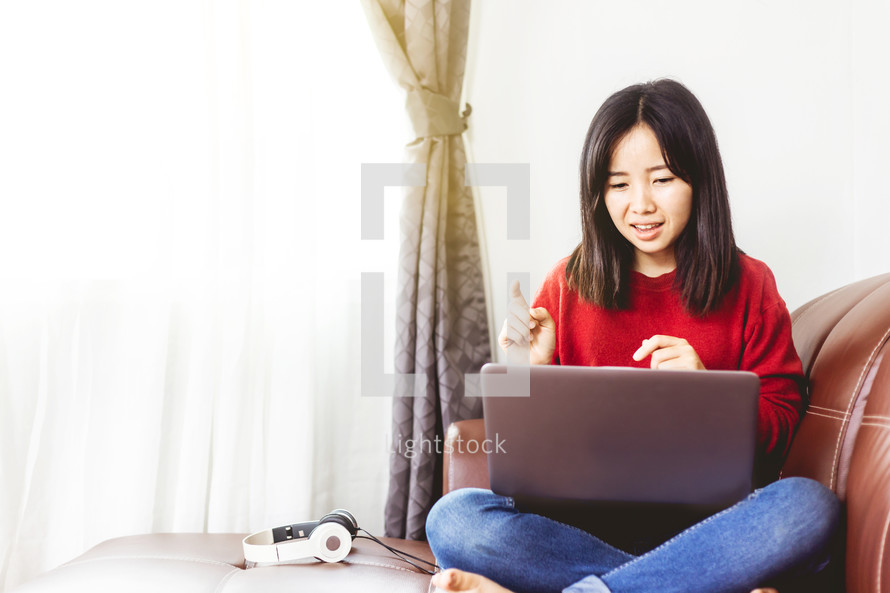 a girl sitting on the couch looking at a laptop 