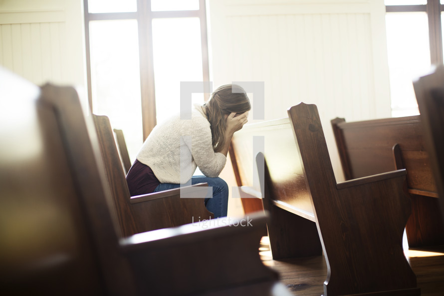 a woman hiding her face sitting in a church pew