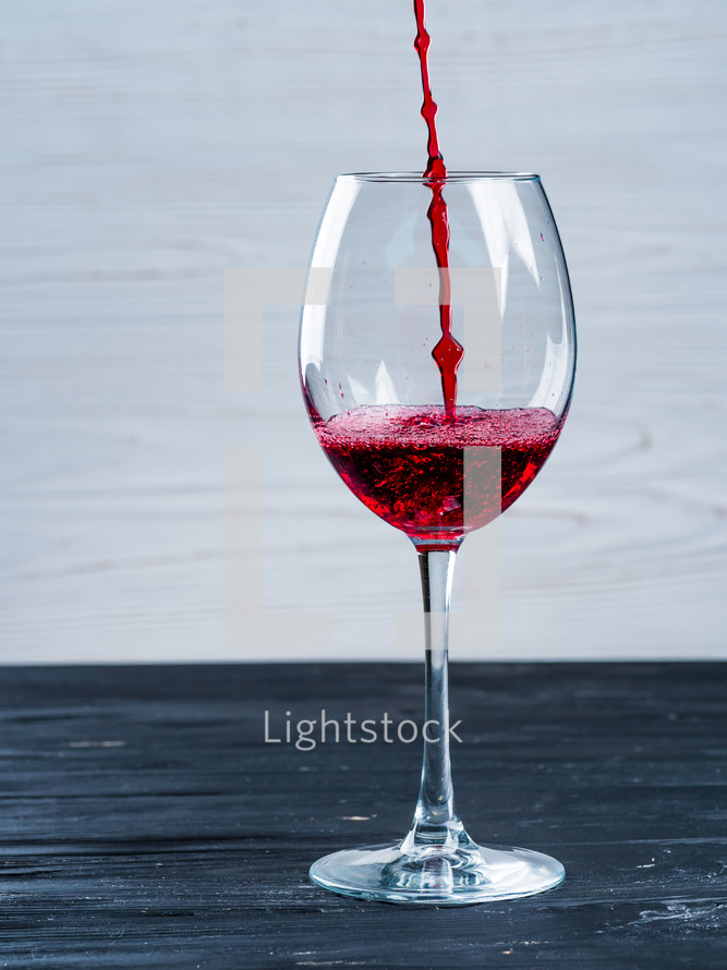 Red wine being poured into wine glass on white background. Minimalist style, black shabby vintage wooden table.