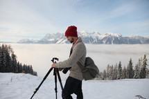 man with a tripod and camera standing outdoors in snow 