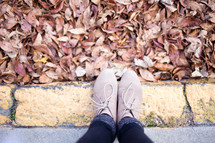 Feet on the curb with autumn leaves.
