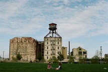 children sitting in the grass and a water tower on an old building 