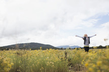 A woman stands in a field of flowers with arms and face raised to the sky.