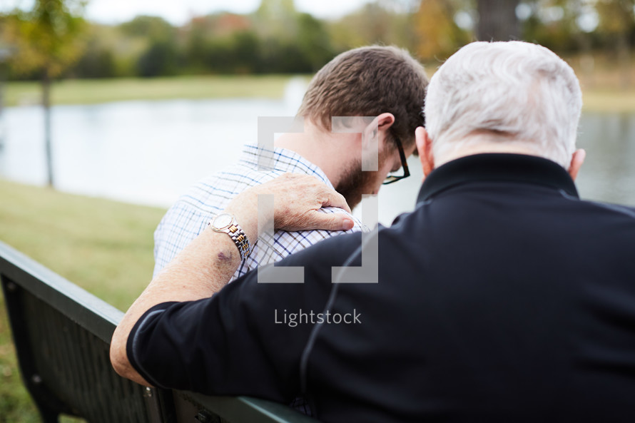 elderly man praying with a young man 