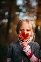a girl holding a fall leaf in front of her face 
