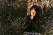 a girl praying in a field under a tree 