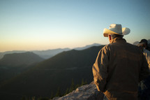 a man in a cowboy hat standing at the top of a mountain 
