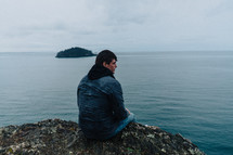 man sitting on a rock looking out at the ocean 