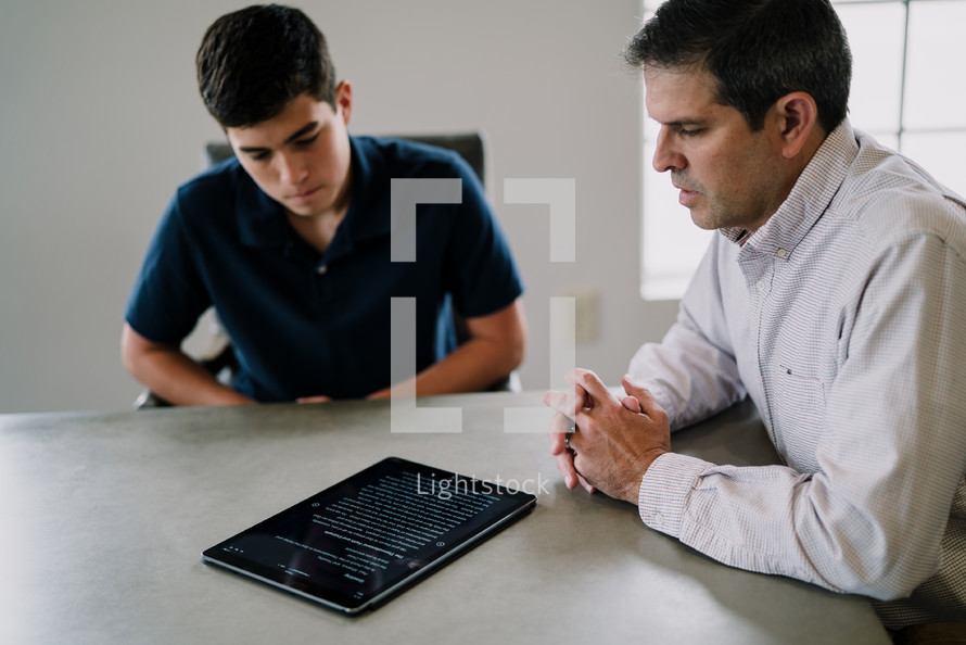 father and son reading Bible verses off of a tablet 