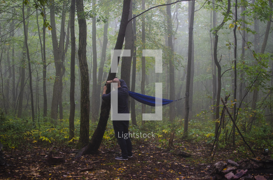 man hanging a hammock in a forest 