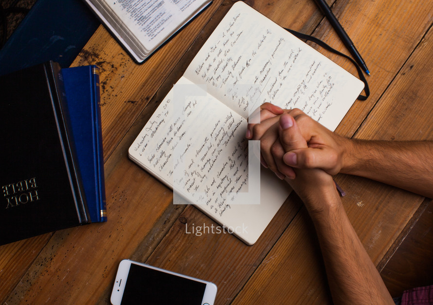 man with praying hands over a journal at a Bible study 