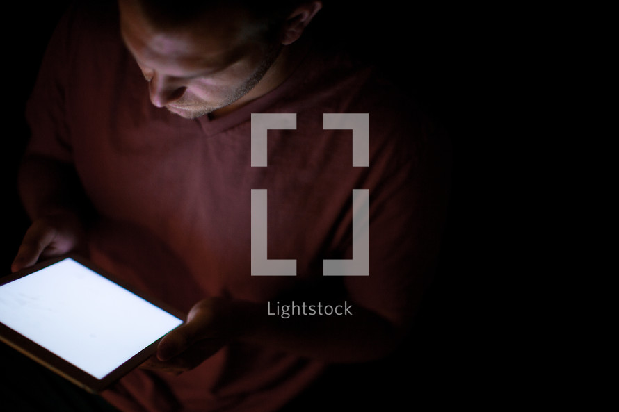 A man holding and being illuminated by an electronic tablet.