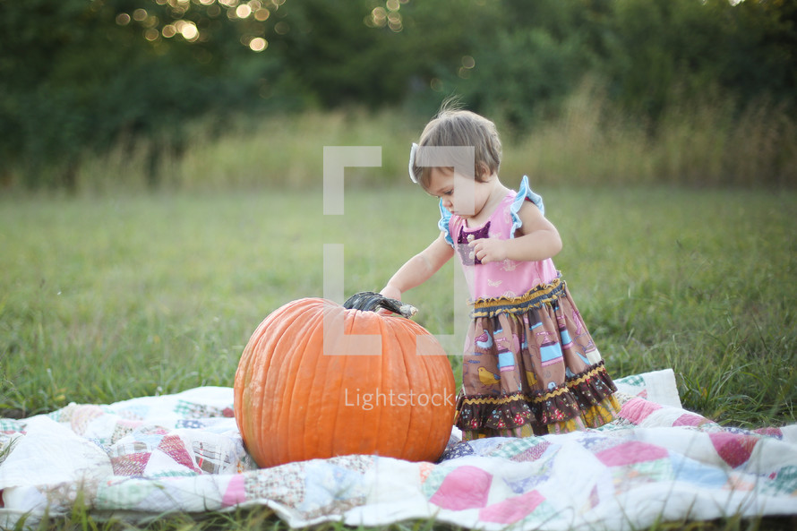 toddler girl on a blanket in the with a pumpkin 