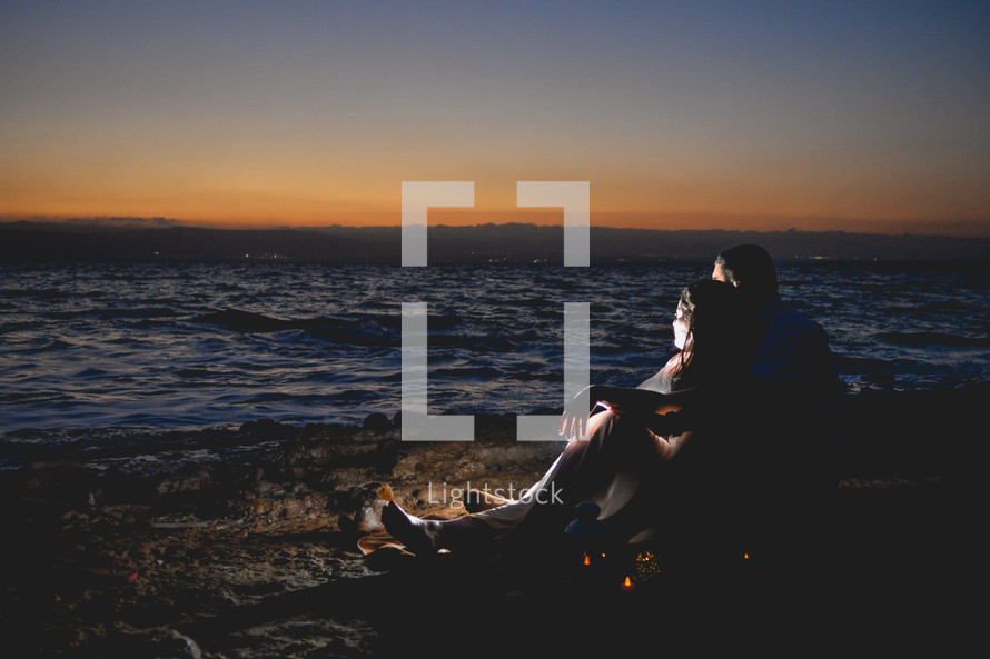 couple snuggling on a beach at night in front of a fire 