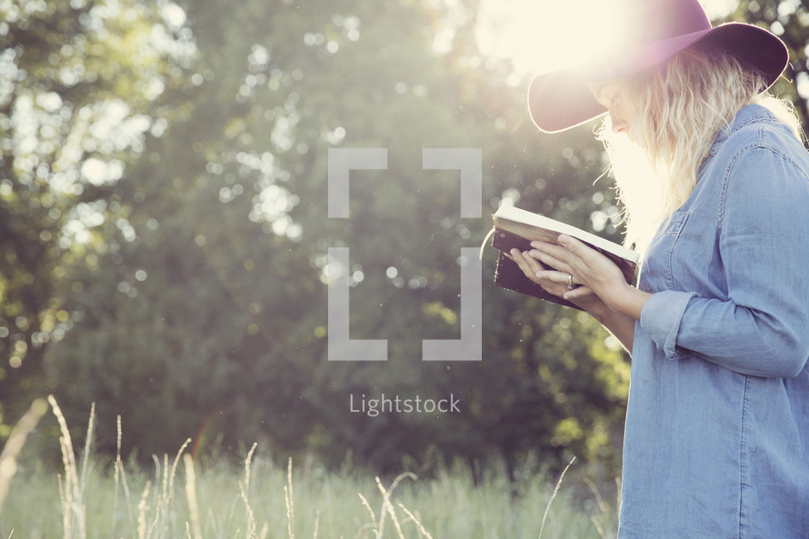 woman holding a book reading under intense sunlight outdoors 