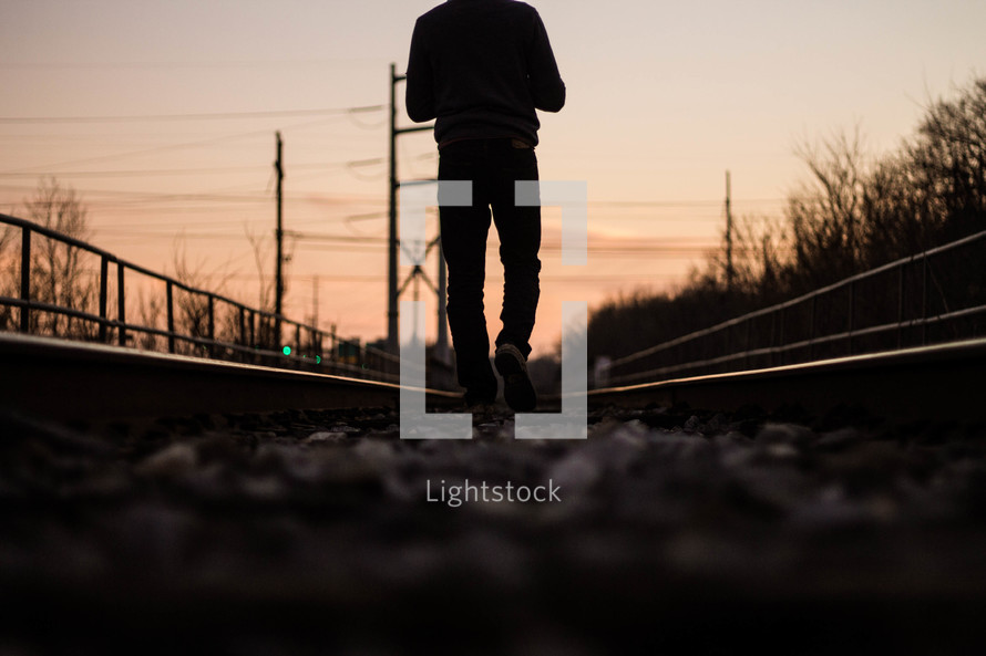 a man walking on train tracks at sunset 