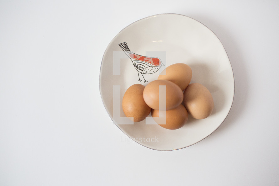 Brown eggs on a white plate with a drawing of a bird.