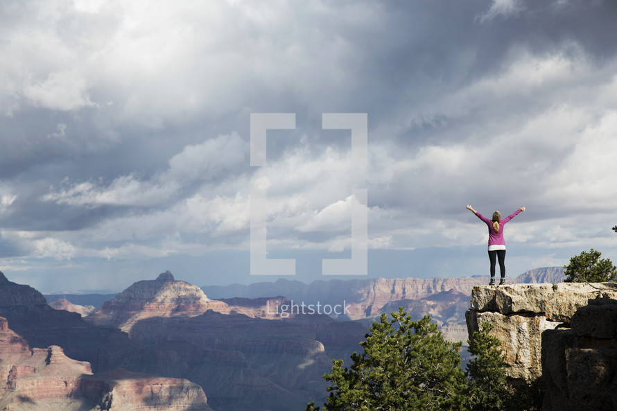 a woman standing at the edge of a cliff with raised arms.