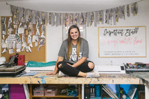 a young woman sitting in a craft room 