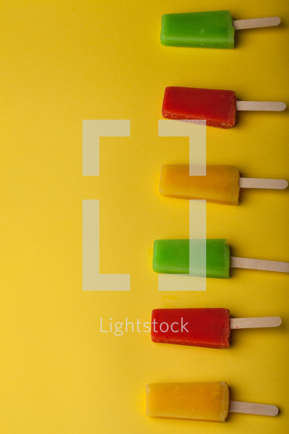 Brightly colored popsicles lined up on a yellow background.