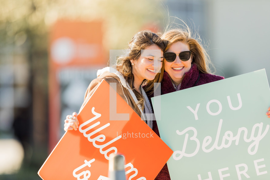 women holding signs - welcome, you belong here 