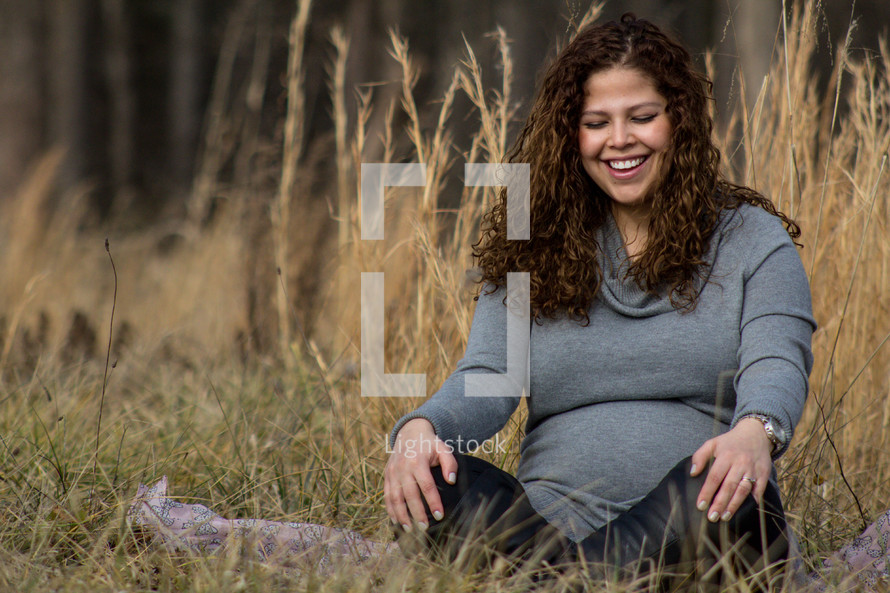 a pregnant woman sitting in a field of tall grass 